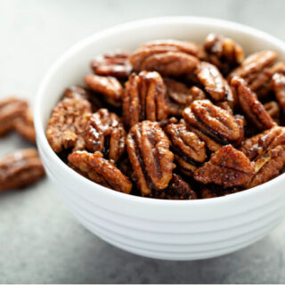 a bowl of sugared pecans on a white background with additional pecans scattered about the bowl