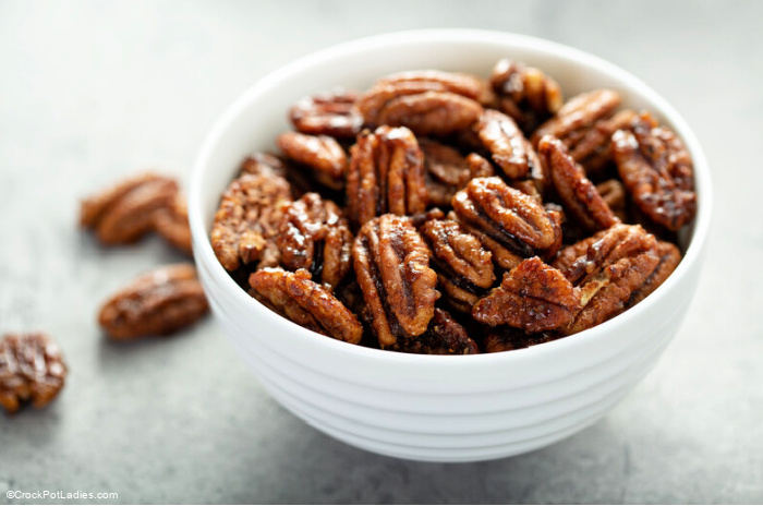 a bowl of sugared pecans on a white background with additional pecans scattered about the bowl